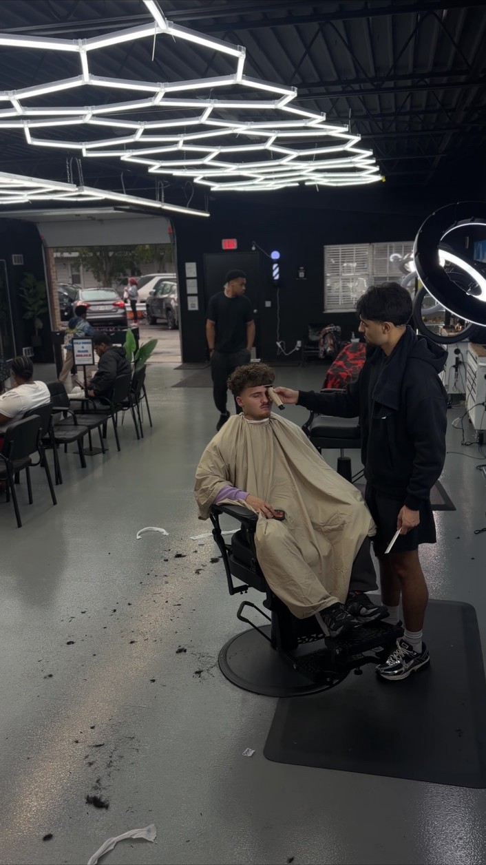 A barber working with a client beneath the shop’s geometric lights